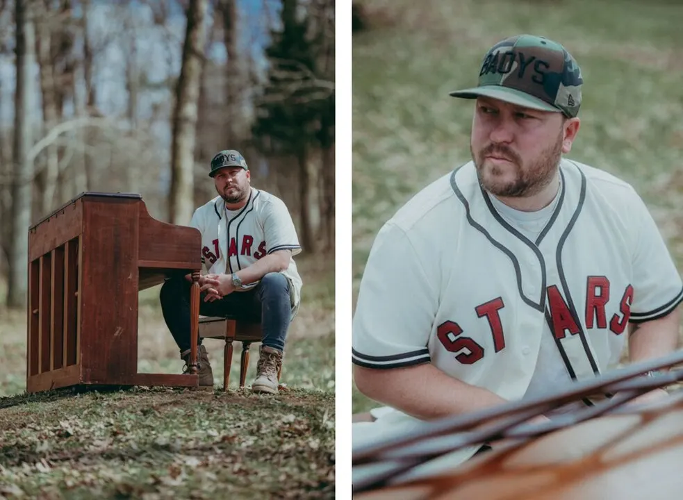 Tenpenny seated at upright piano in wooded grass area wearing STARS shirt.